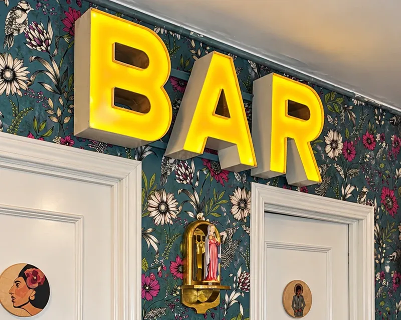 El BAR de neón sobre el papel pintado de flores de El Amor Hermoso