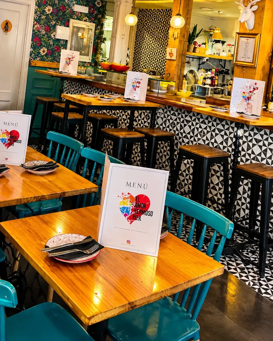Mesas y barra de El Amor Hermoso Bar, con sus sillas turquesa y la carta en cada mesa